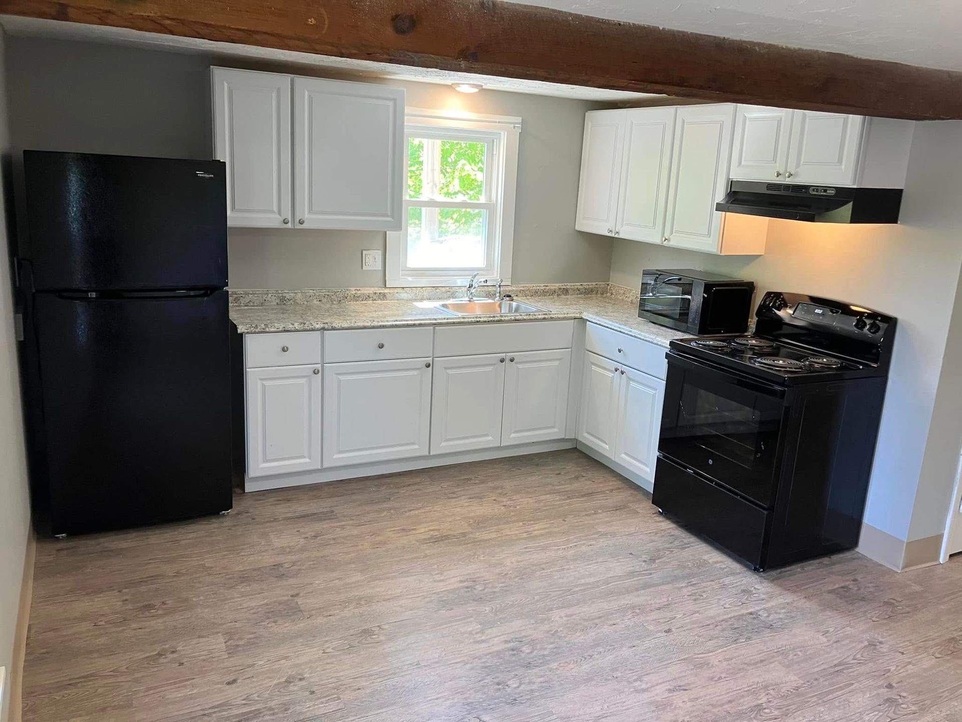 A kitchen with white cabinets , a black refrigerator , a black stove , and a microwave.