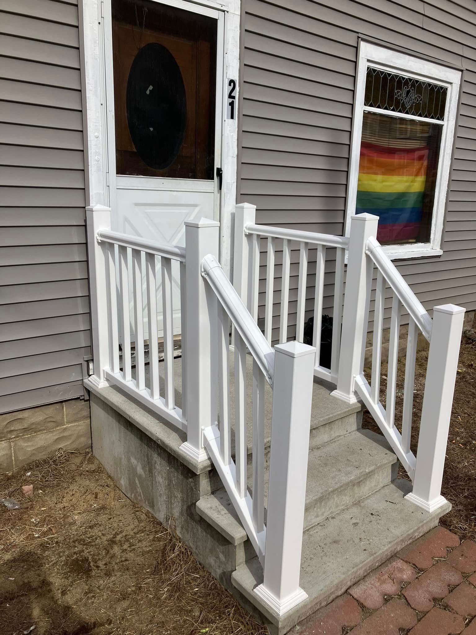A white porch with stairs and a rainbow flag in the window.