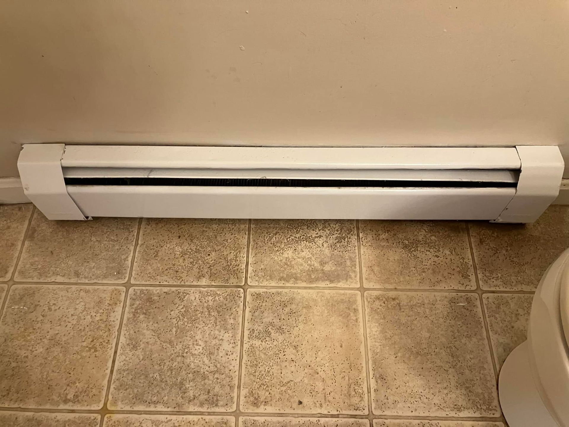 A white heater is sitting on a tiled floor next to a toilet.