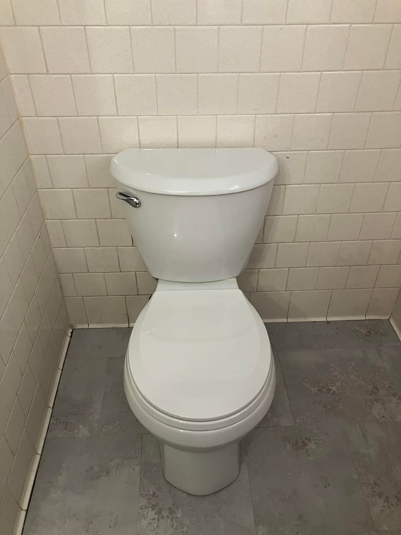 A white toilet is sitting in a bathroom next to a brick wall.