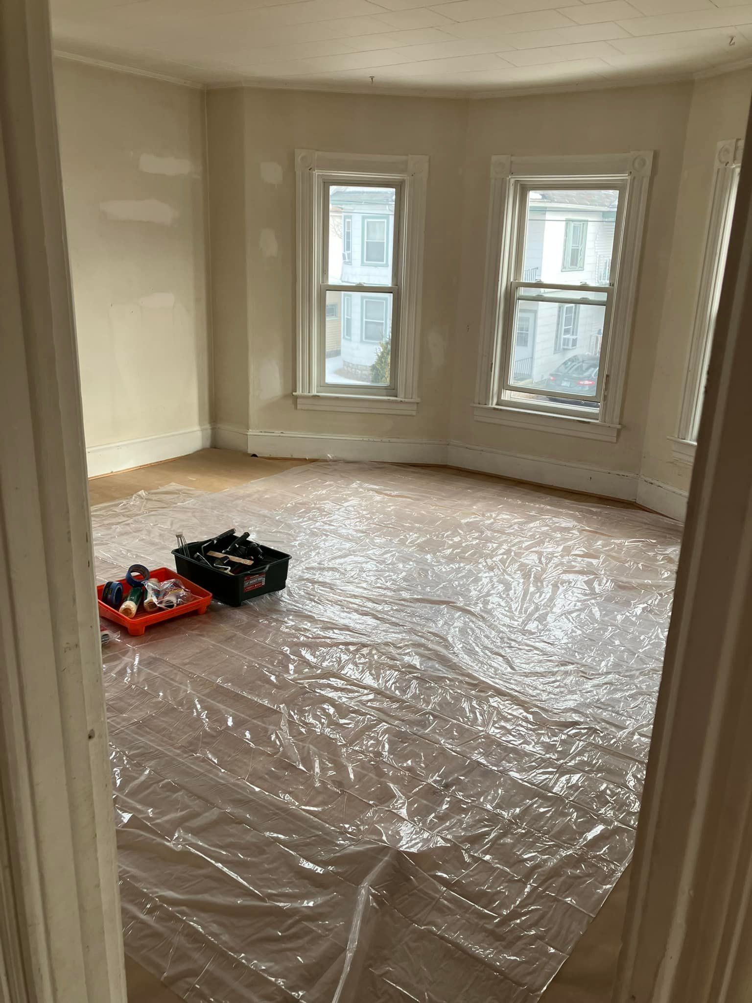 An empty room with a plastic sheet on the floor and two windows.