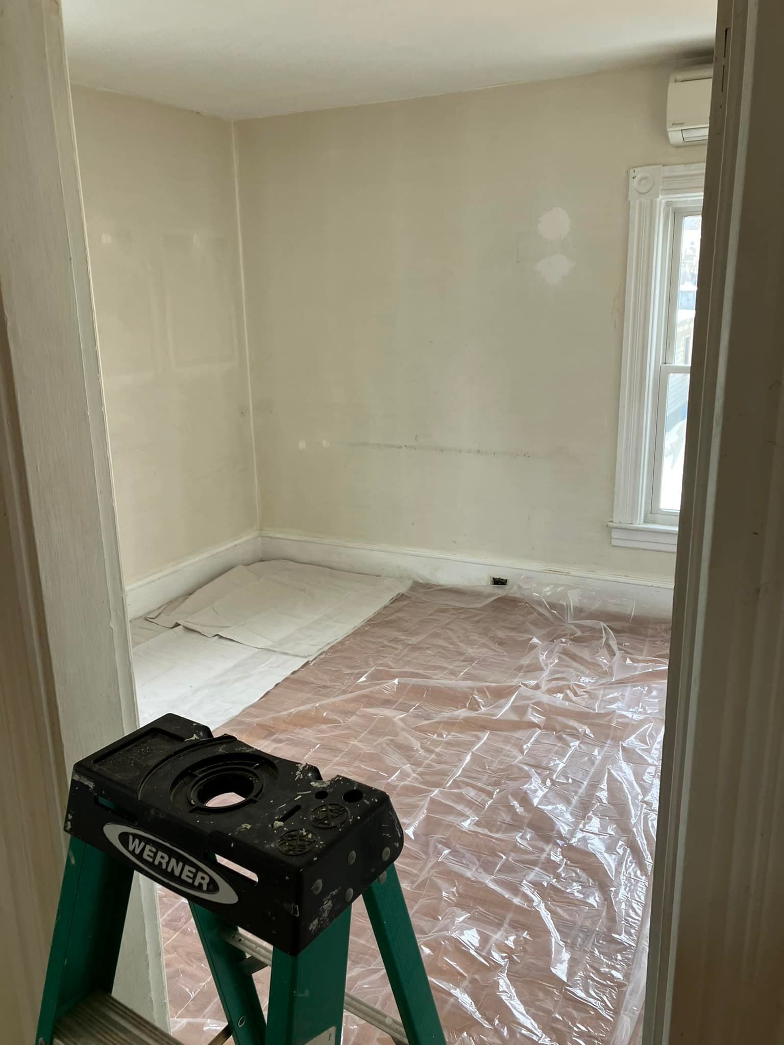 A room with a ladder and plastic covering the floor.