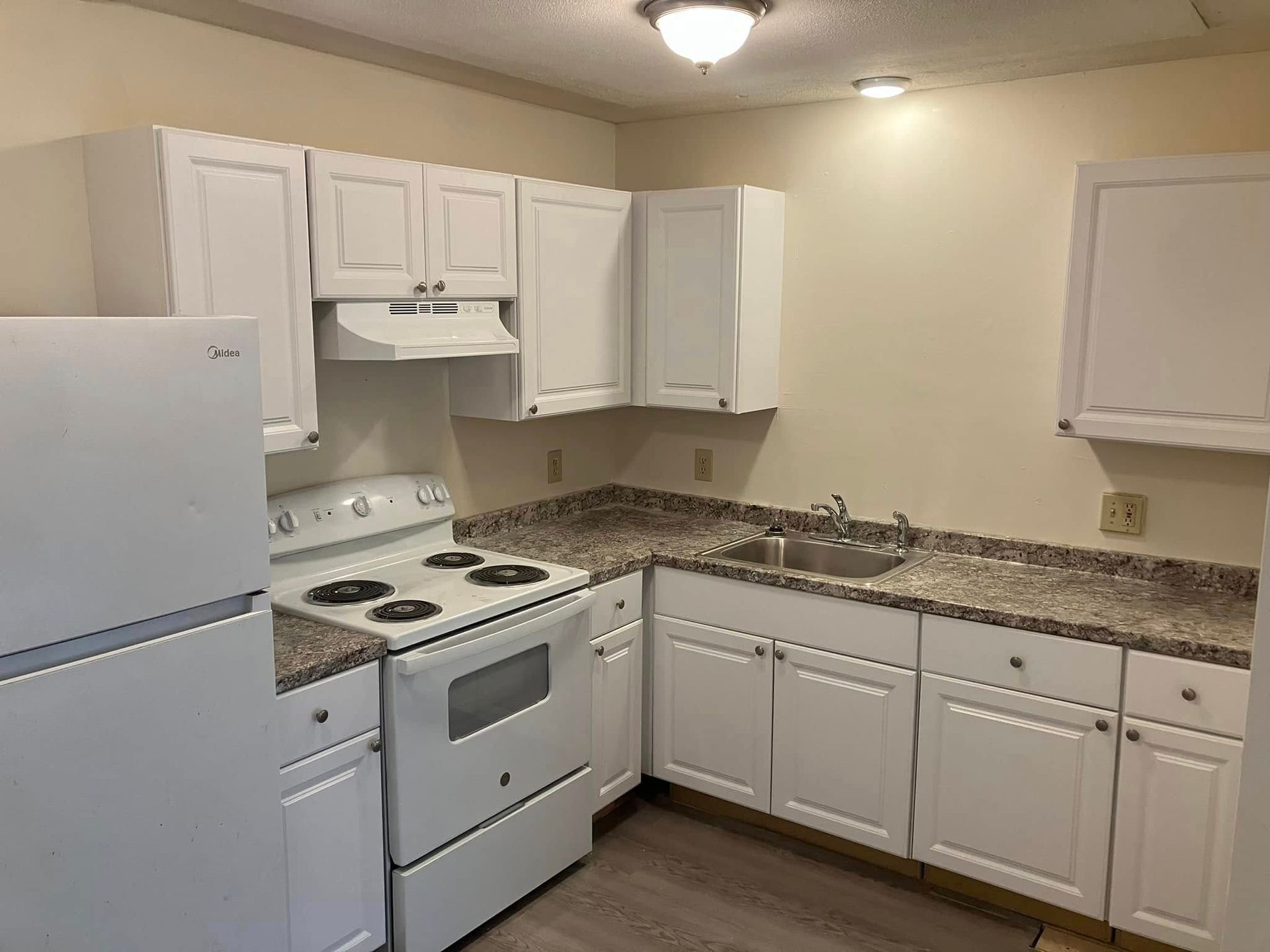 A kitchen with white cabinets , a stove , a refrigerator , and a sink.