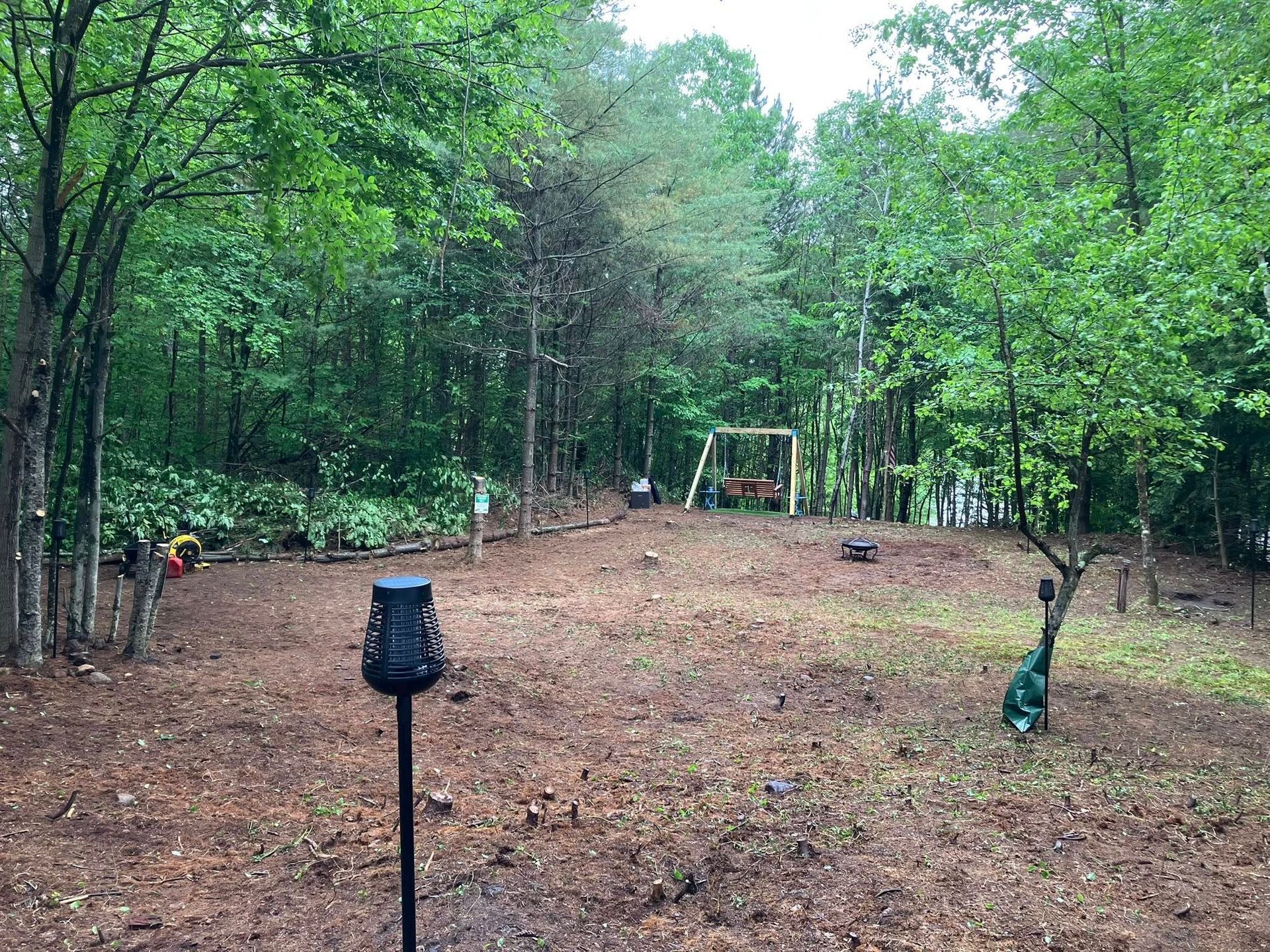 A dirt field with trees and a swing set in the background.