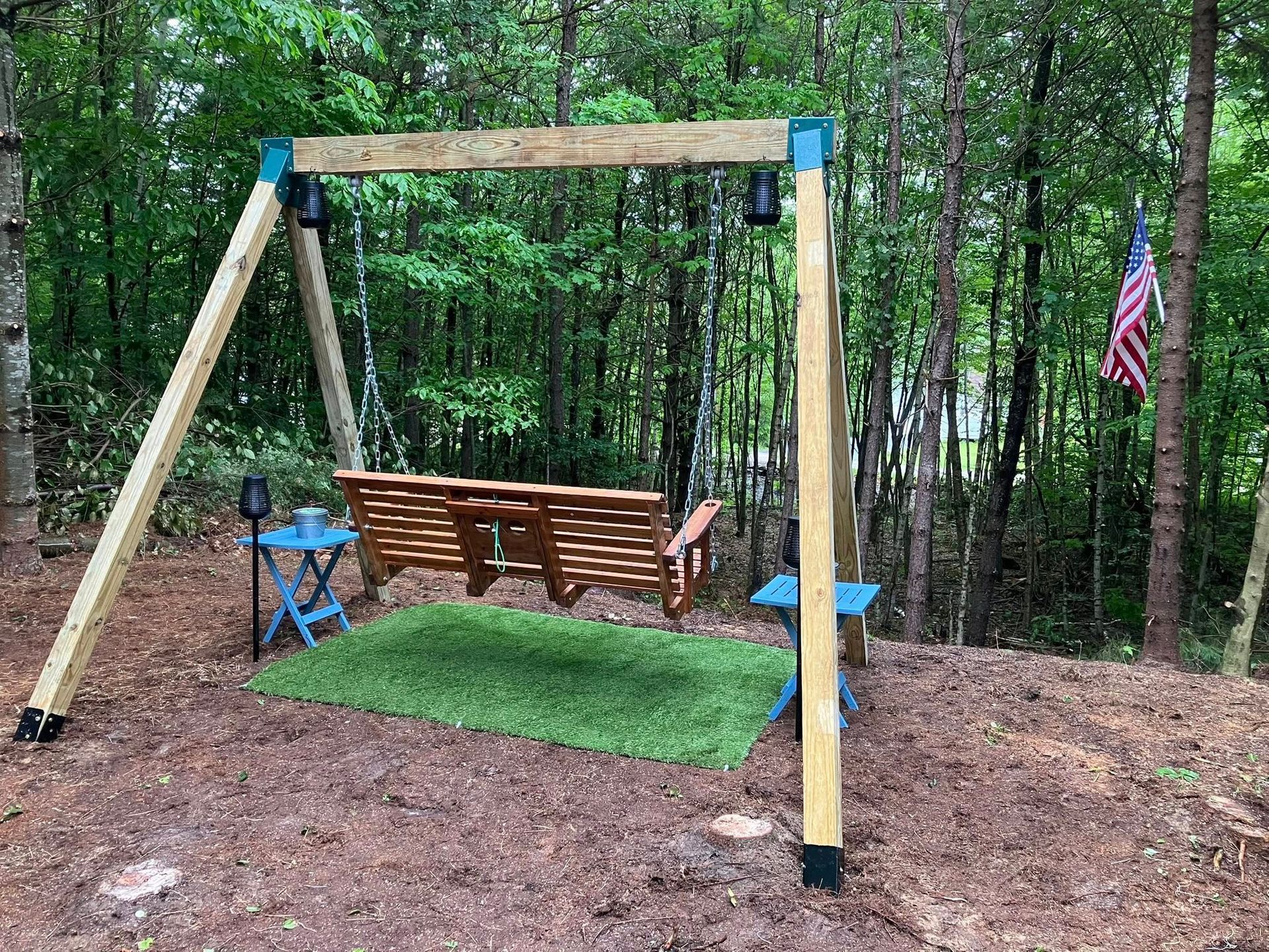 A wooden swing is sitting in the middle of a forest.