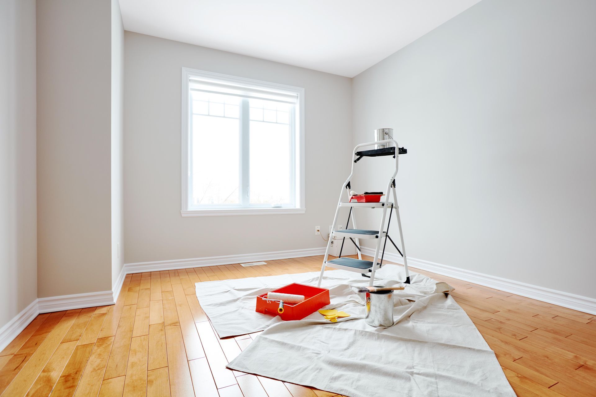 An empty room with a ladder and paint on the floor.