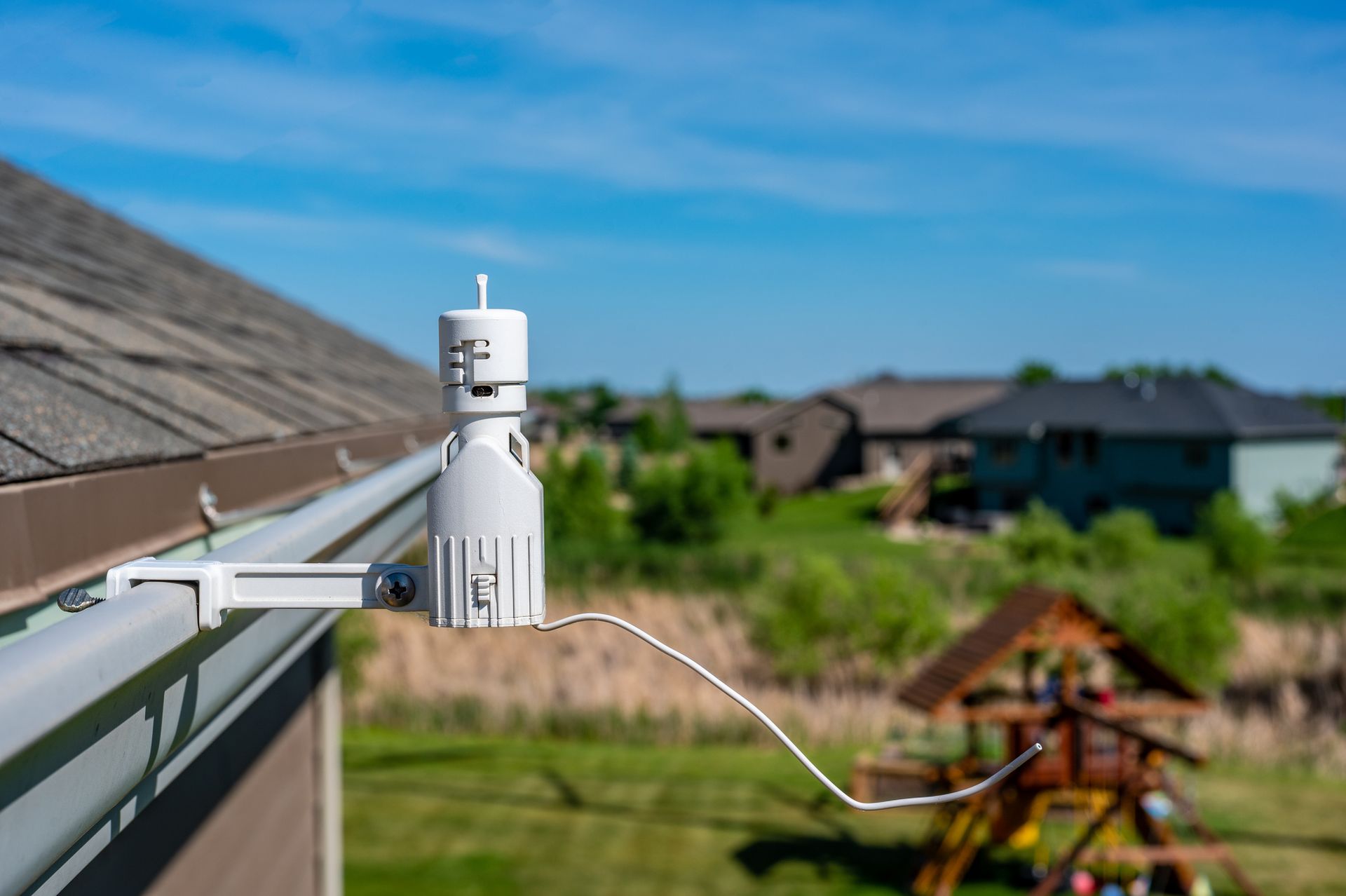 A rain gauge is attached to a gutter on the side of a house.