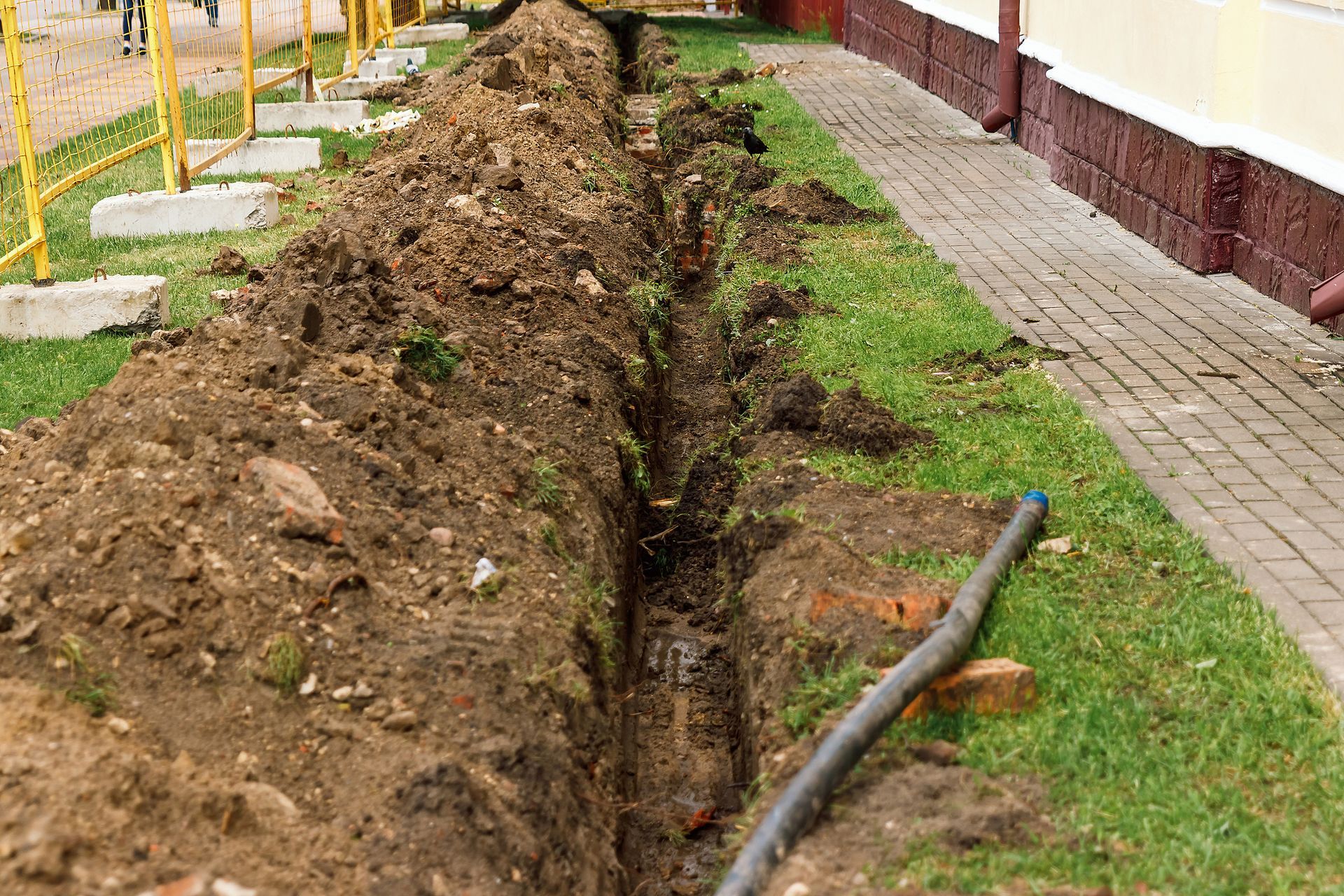 A trench is being dug in the grass next to a sidewalk.
