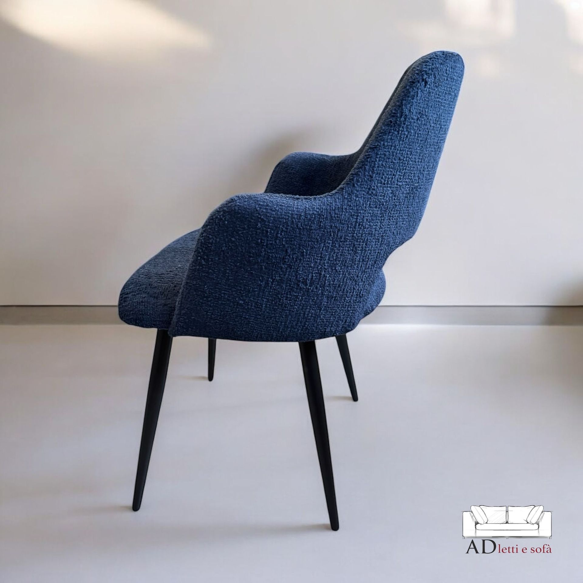 Una sedia blu con le gambe nere è appoggiata su un pavimento bianco