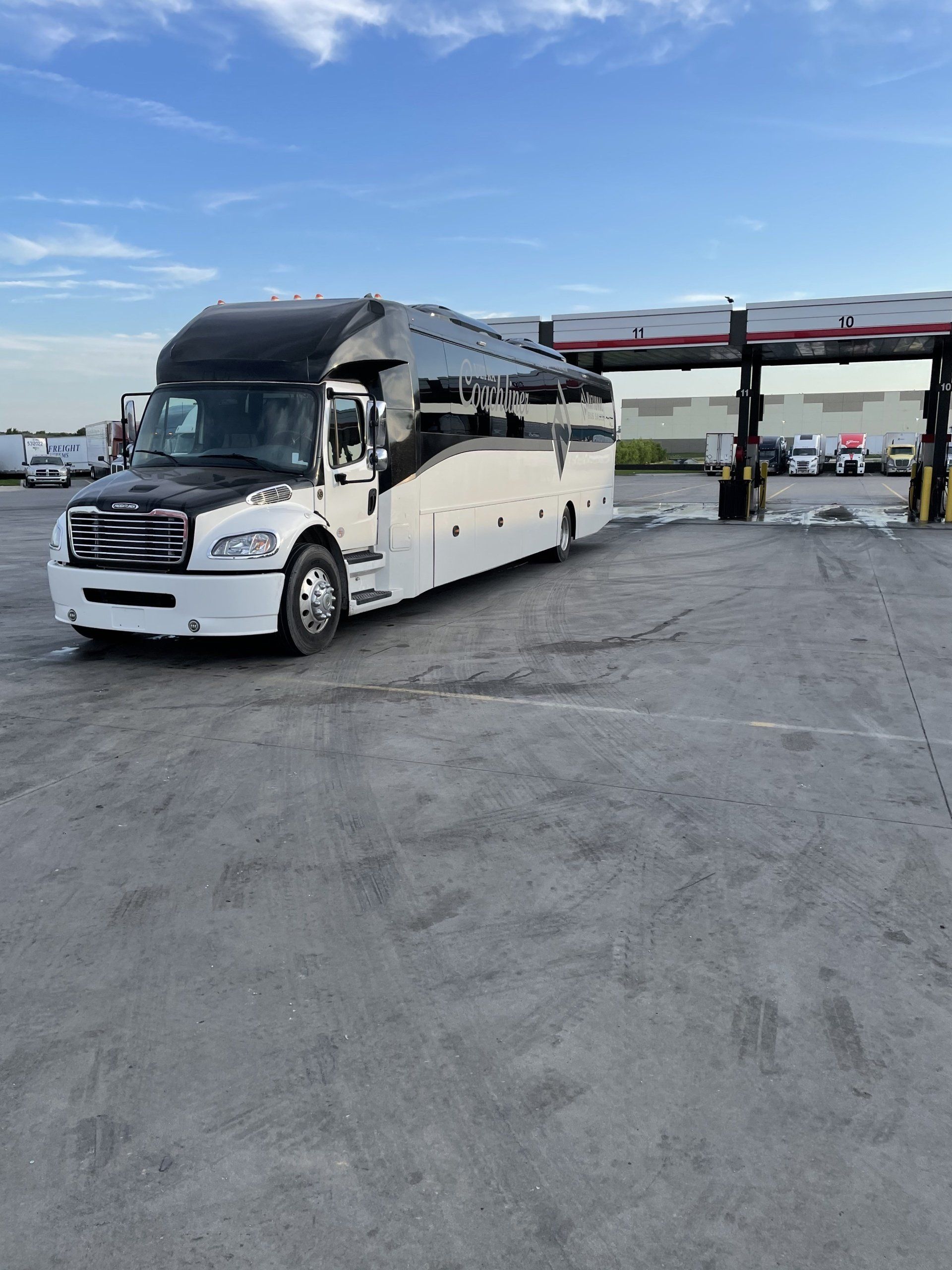 A large bus is parked in a parking lot next to a gas station