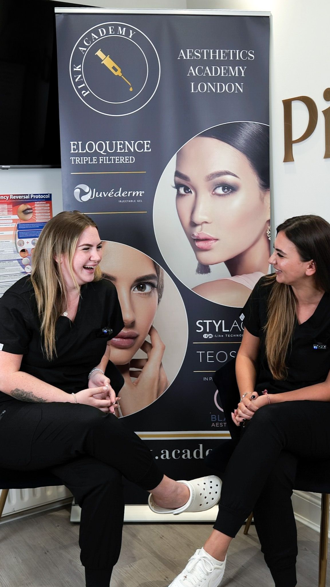 Two women are sitting next to each other in front of a banner.