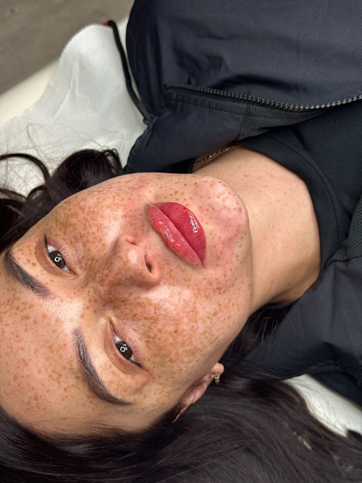A woman with freckles and red lips is laying on her back.