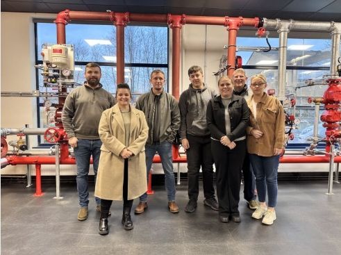 A group of people are posing for a picture in a room with red pipes.