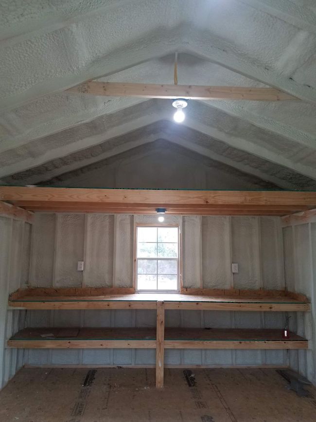 A person in protective gear installs a white vapor barrier against the walls and floor of a crawl space.