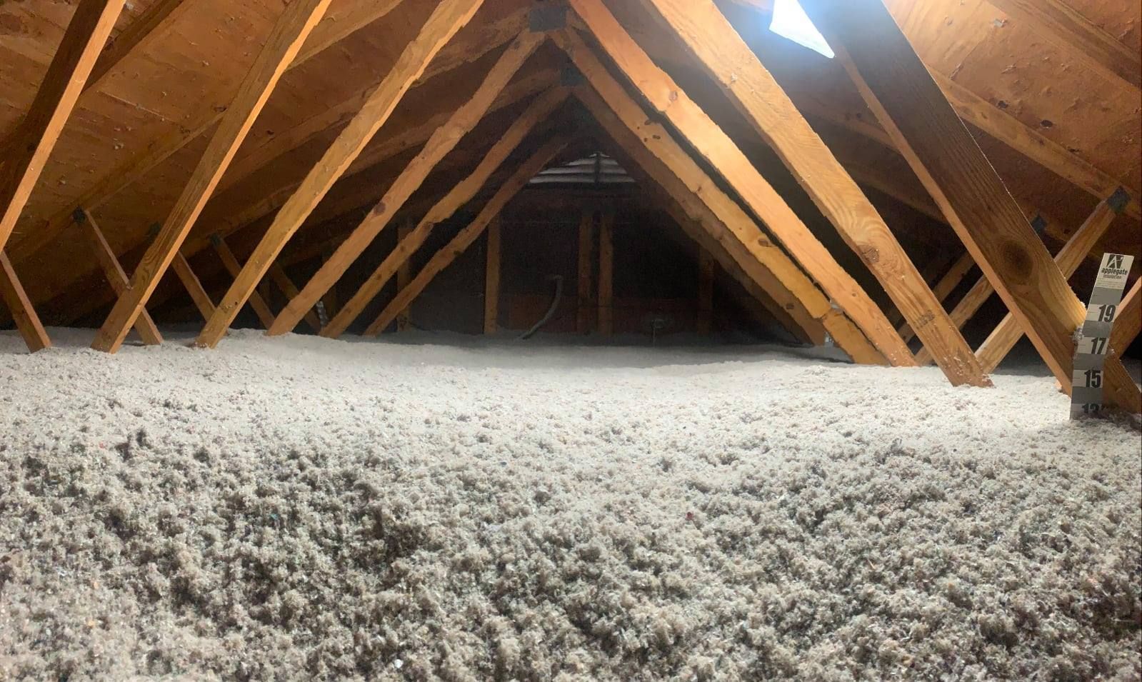 An attic with a thick, even layer of grey blown-in insulation between the wooden rafters.