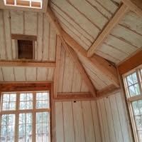 A room with light wood paneling, exposed structural beams, and large windows with a view of trees outside.