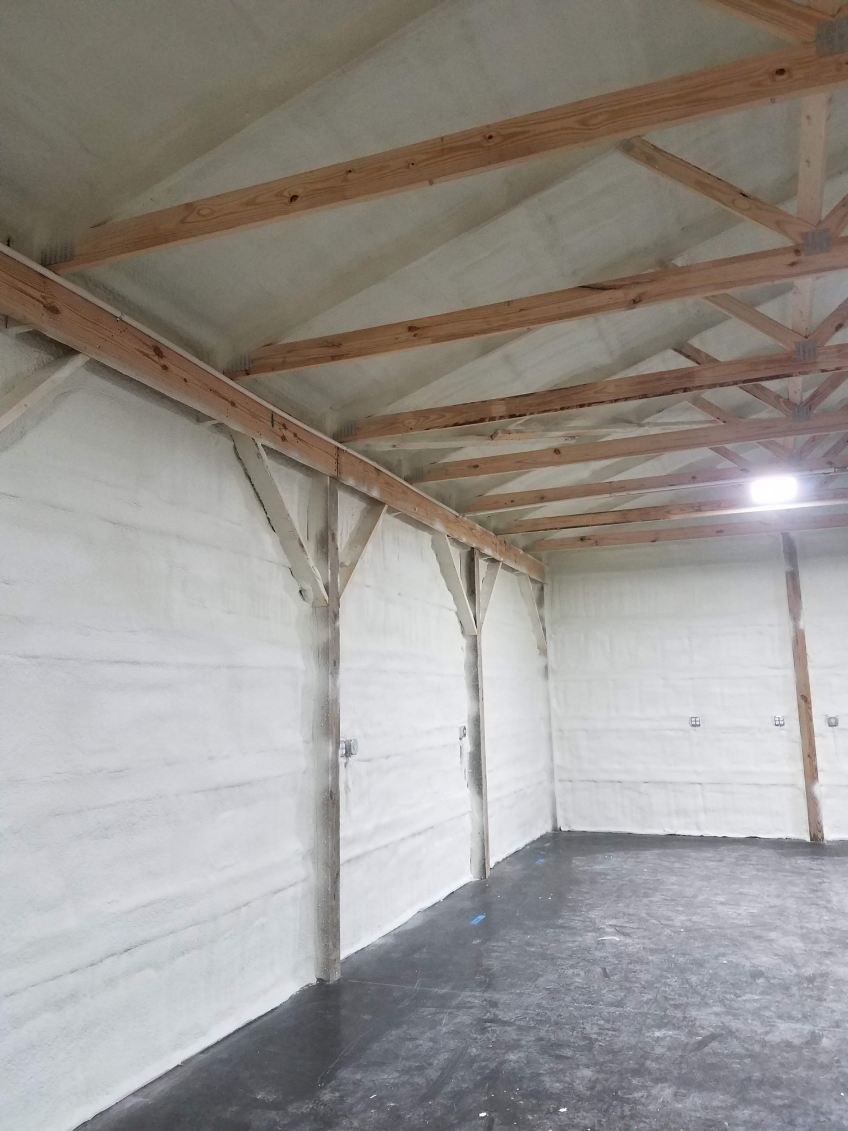 An interior view of a wooden attic frame with foam insulation between beams and a square skylight open to the sky.