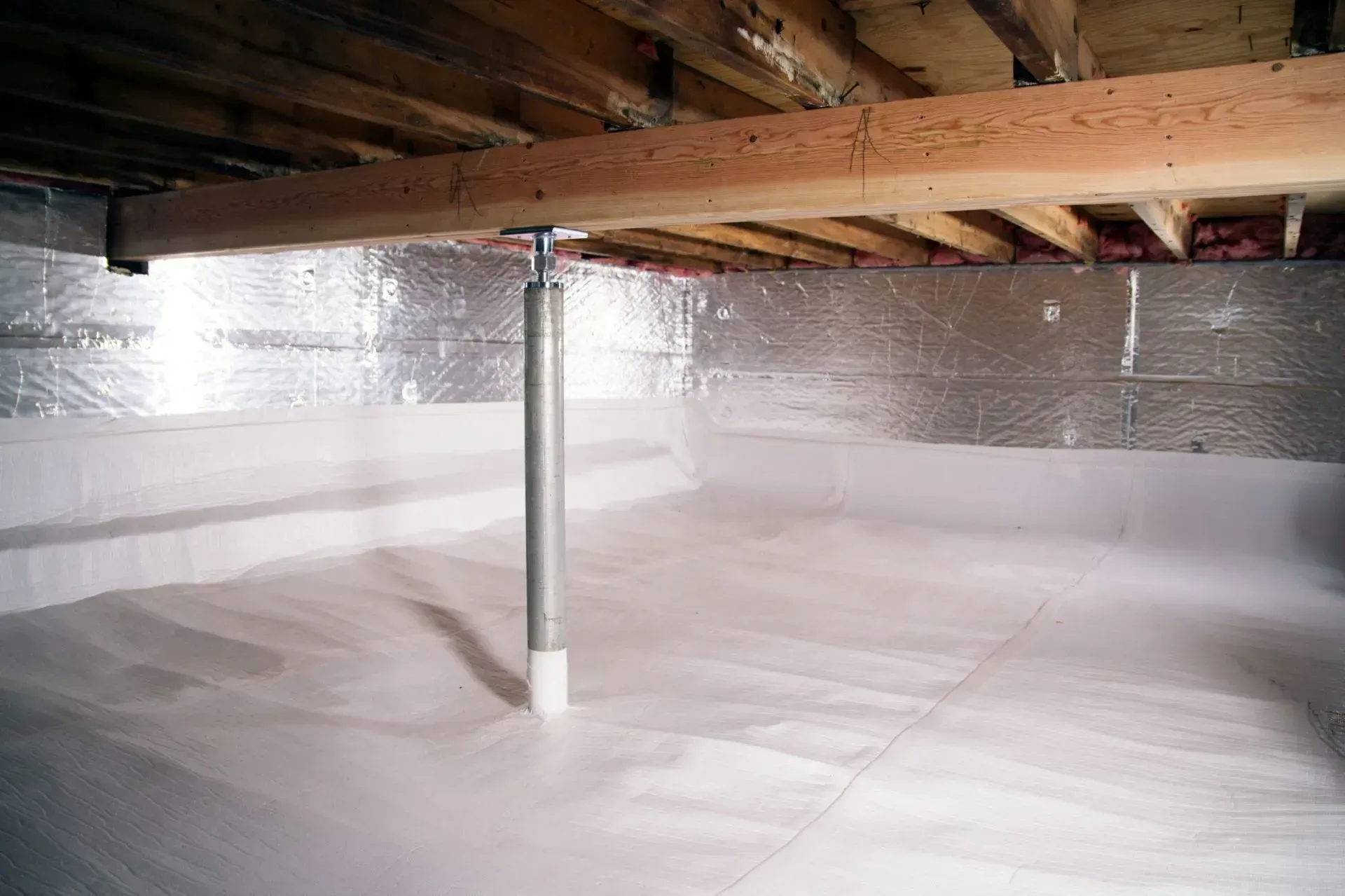 An interior view of a wooden attic frame with foam insulation between beams and a square skylight open to the sky.