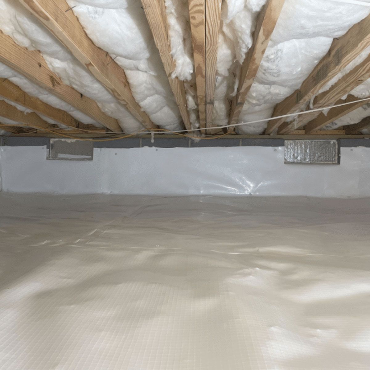 An interior view of a wooden attic frame with foam insulation between beams and a square skylight open to the sky.