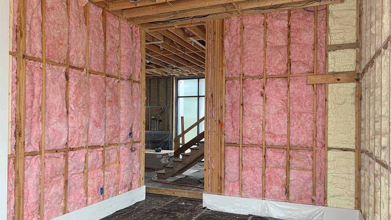 Interior construction view of wall studs with pink fiberglass and yellow spray foam insulation in a partially finished home.