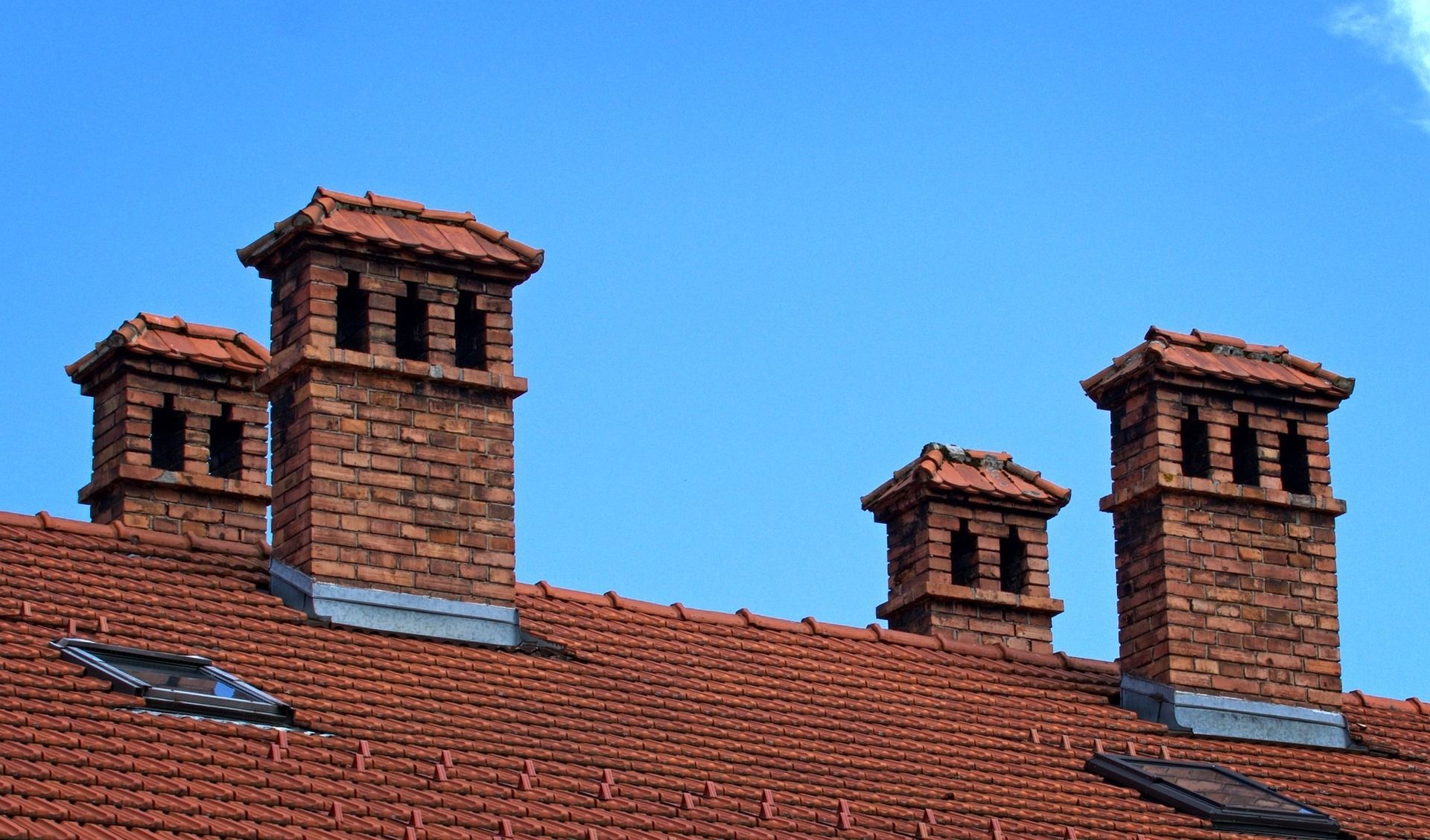 Three Chimneys On Top Of A Red Tiled Roof