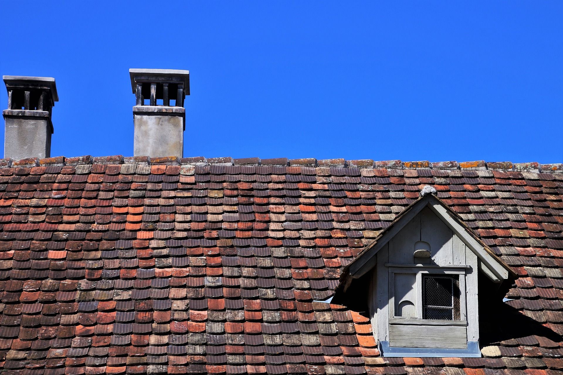 A Roof With Two Chimneys And A Small Window