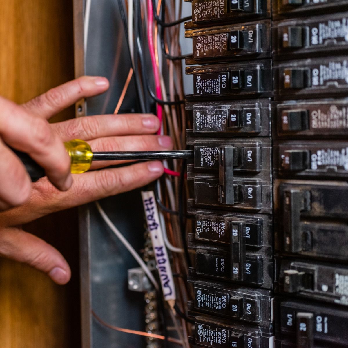 A person is using a screwdriver to fix an electrical panel.