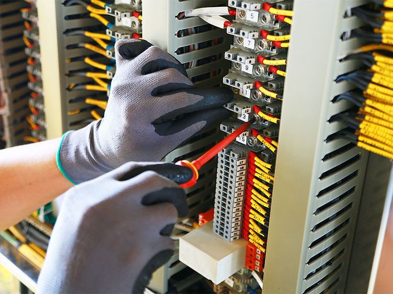 A person is working on an electrical box with a screwdriver.