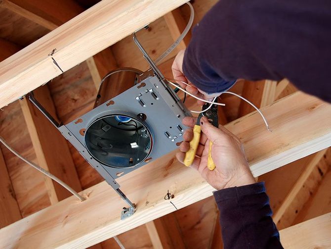 A person is working on a light fixture in the ceiling of a house.