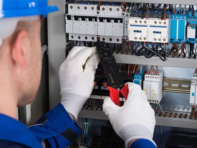 An electrician is working on a circuit board with a tool.