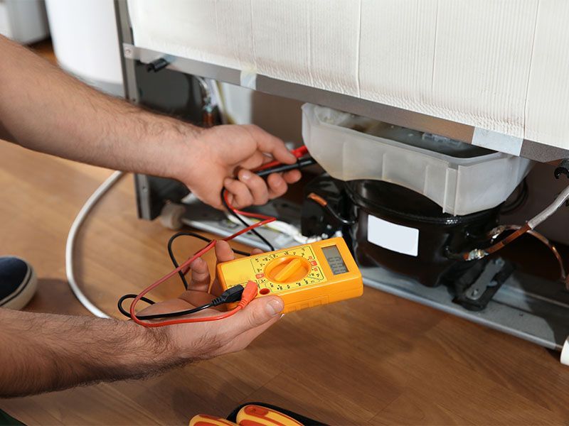 A man is fixing a refrigerator with a multimeter.