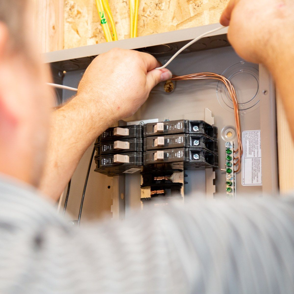 A man is working on a electrical box with wires coming out of it.