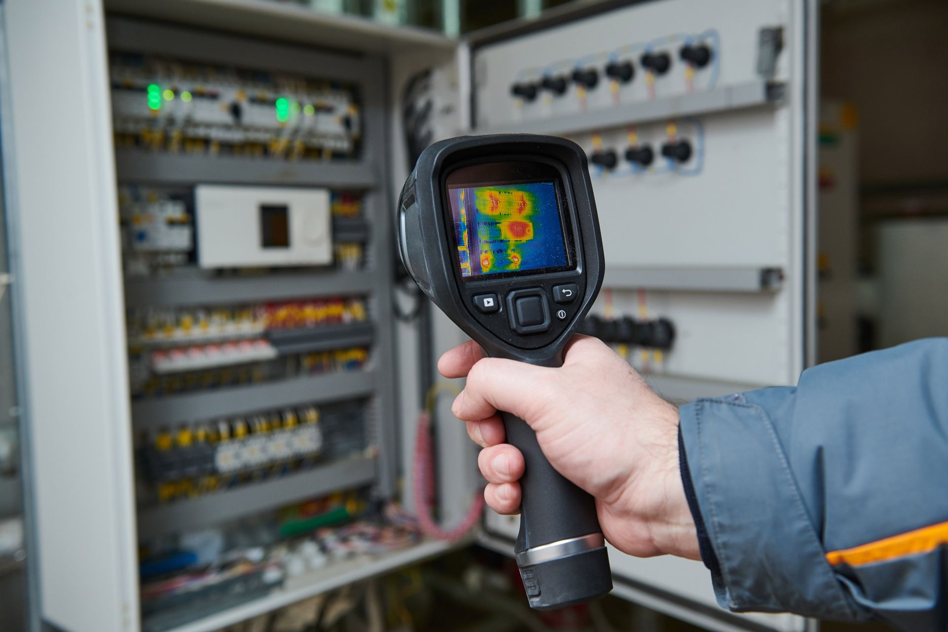 A person is holding a thermal camera in front of an electrical box.