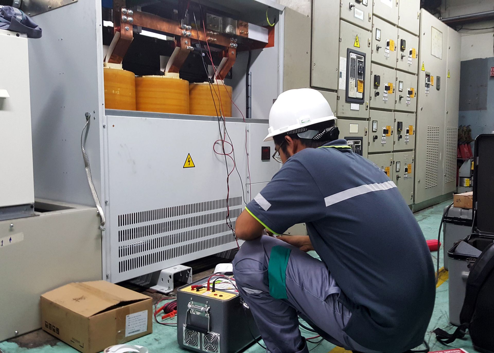 A man is kneeling in front of a transformer in a room.