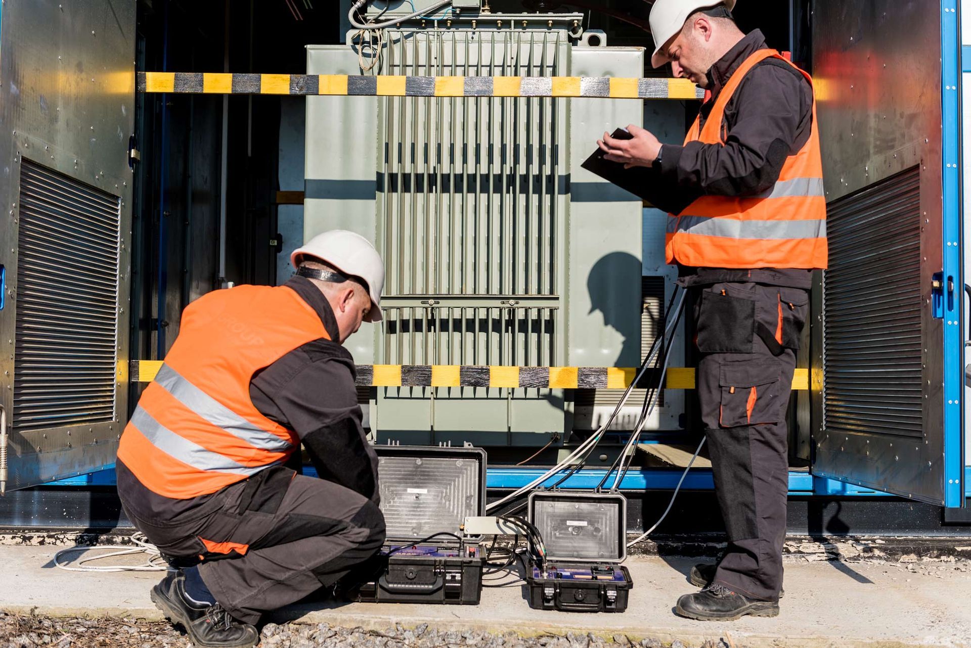 Two men are working on a transformer outside of a building.