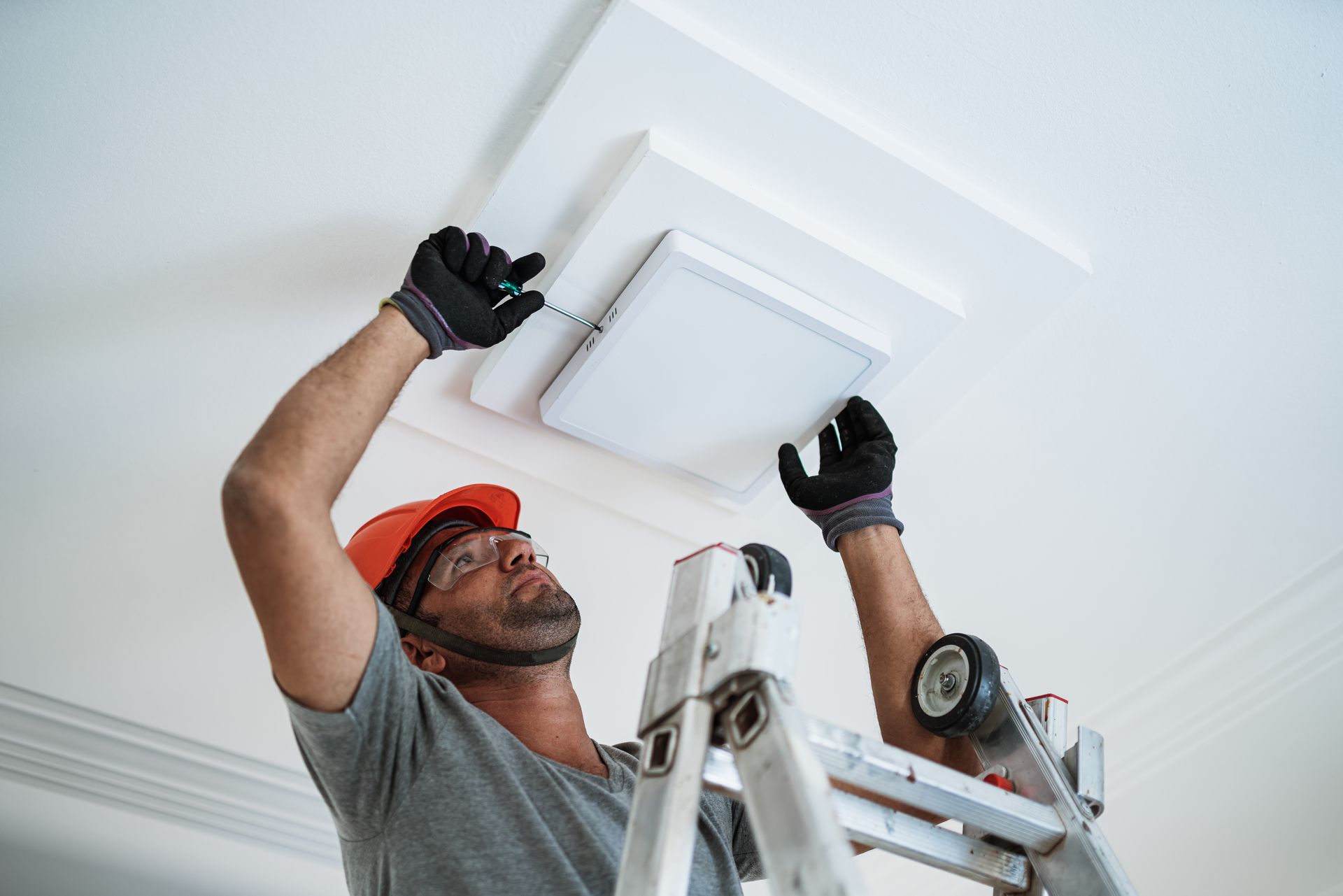 An electrician, wearing an orange helmet, is performing an LED lighting installation on the ceiling.