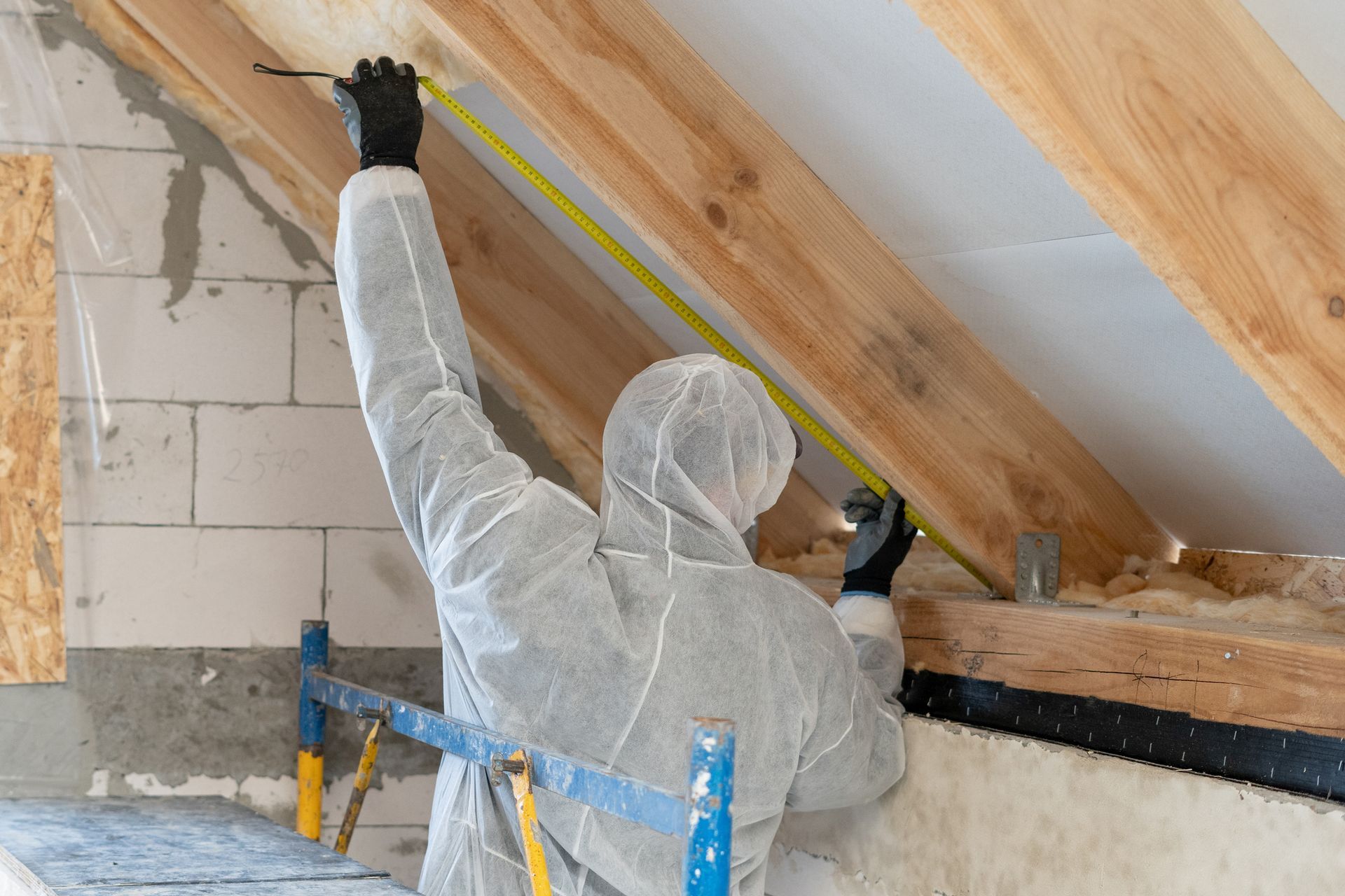 Worker applying insulation to a ceiling with protective gear and suit