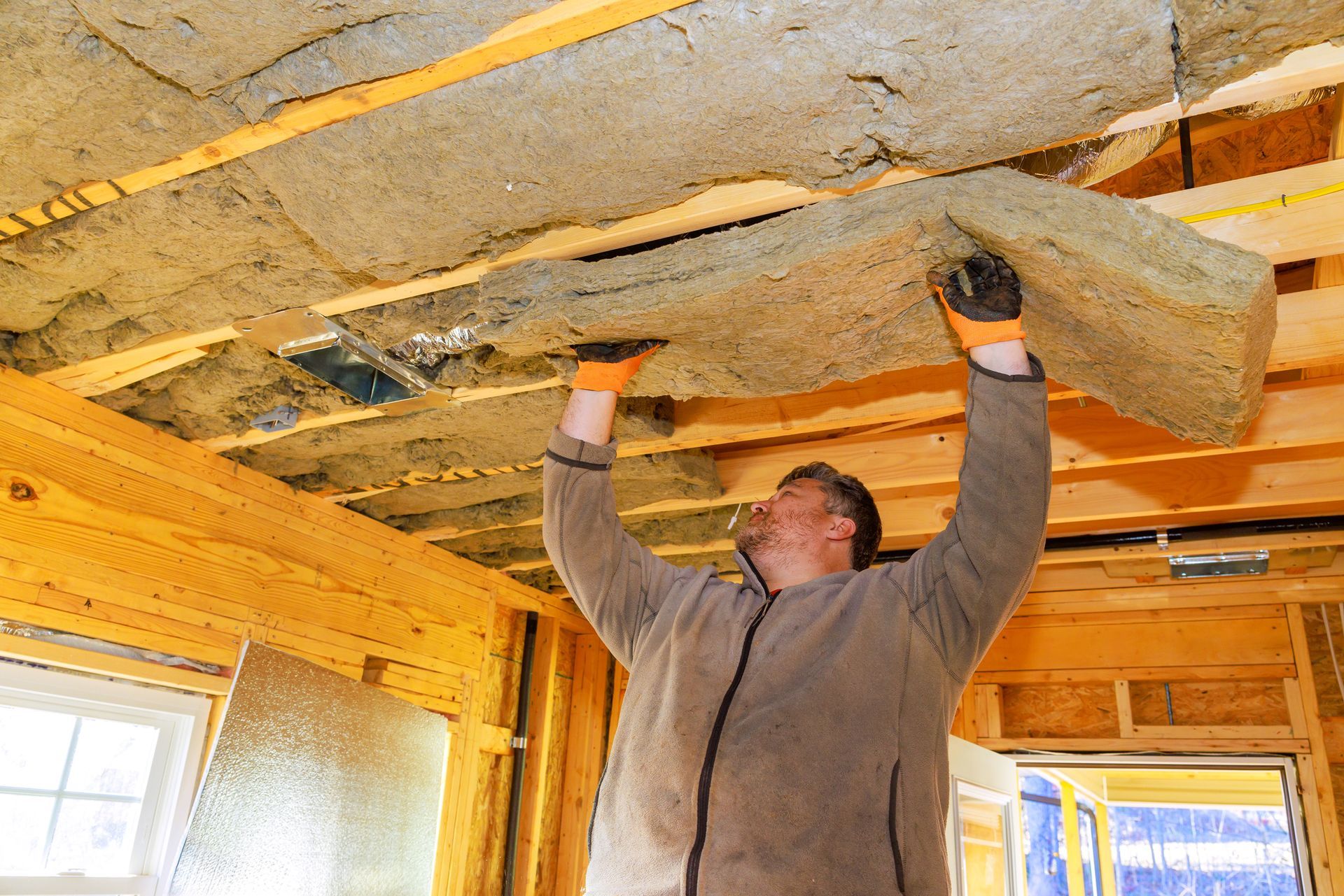 A professional insulation installer fitting ceiling insulation in a residential home.