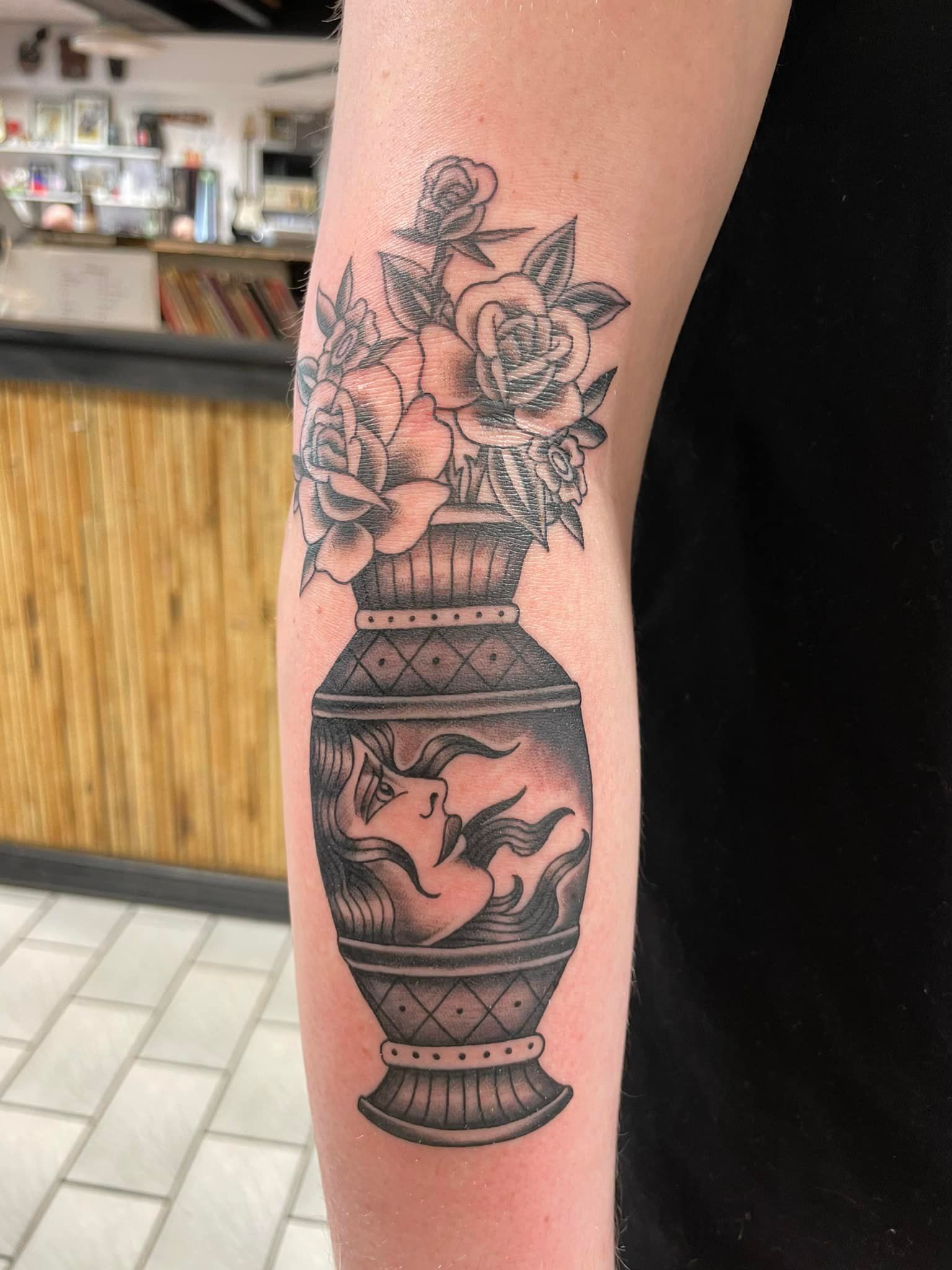 Sort og grå tatovering av dekorativ urne med kvinnelig profil og blomster – på underarm
