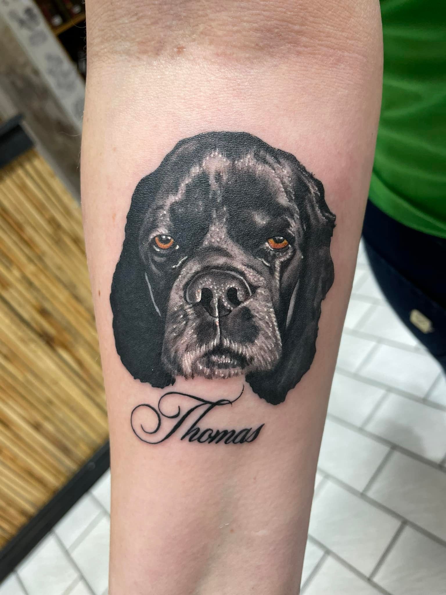 Realistisk tatovering av svart hund med navnet Thomas i kursiv under – på underarm