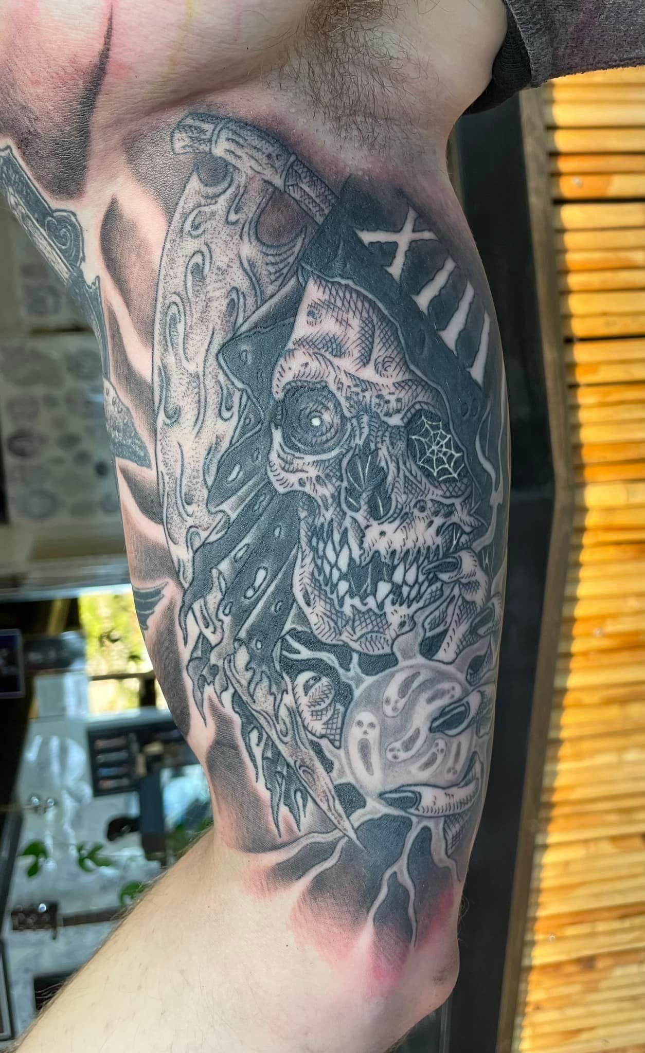 Black & grey tatovering av demonisk hodeskalle med romertall XIII og spøkelsesdetaljer – på overarm