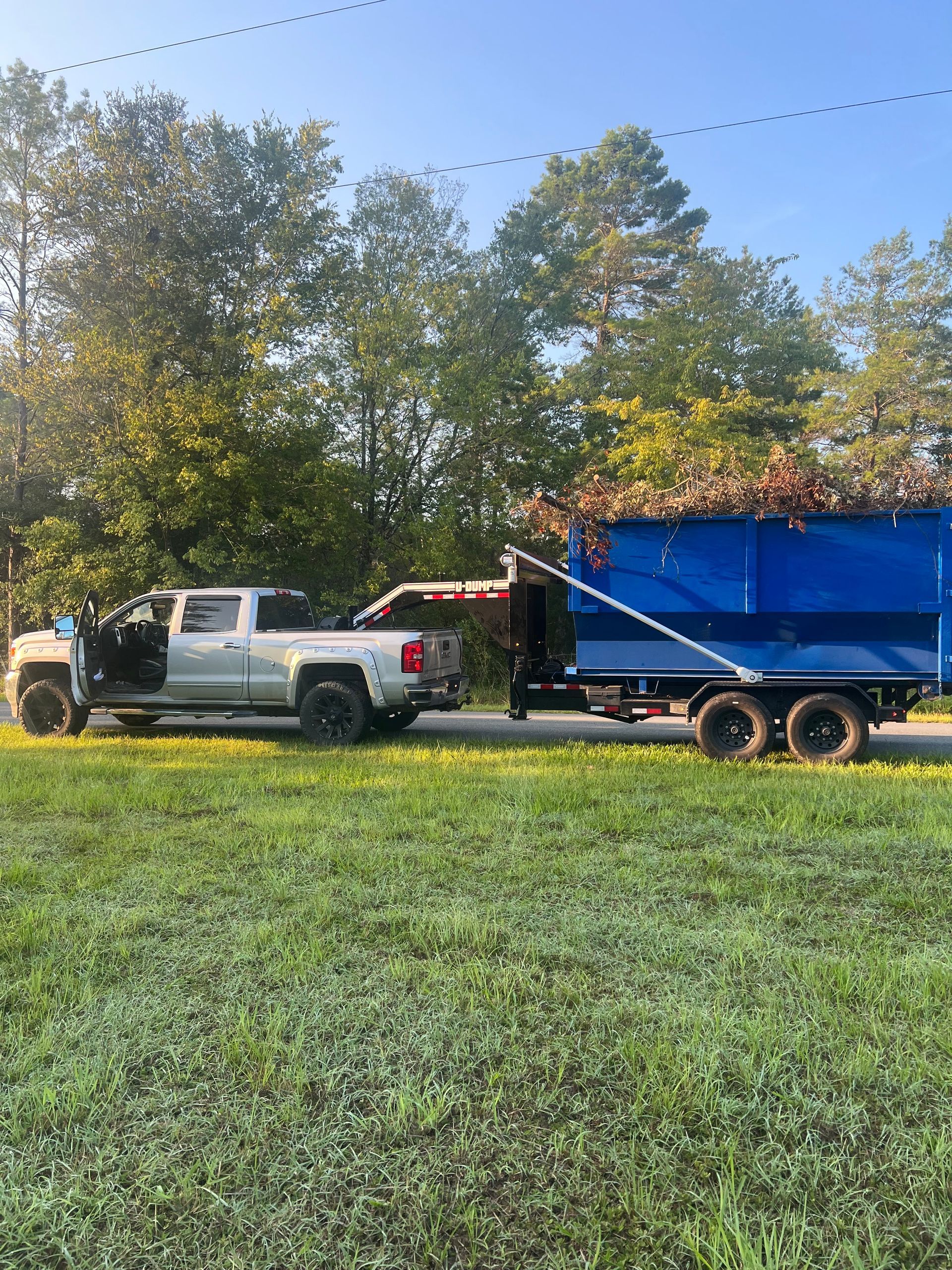 A white truck is towing a blue dumpster in a grassy field.