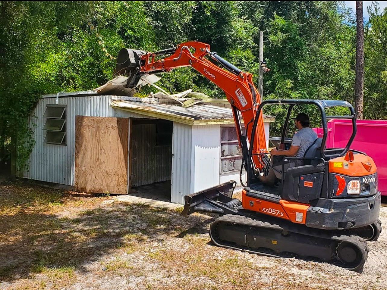 A man is driving a small excavator next to a shed.