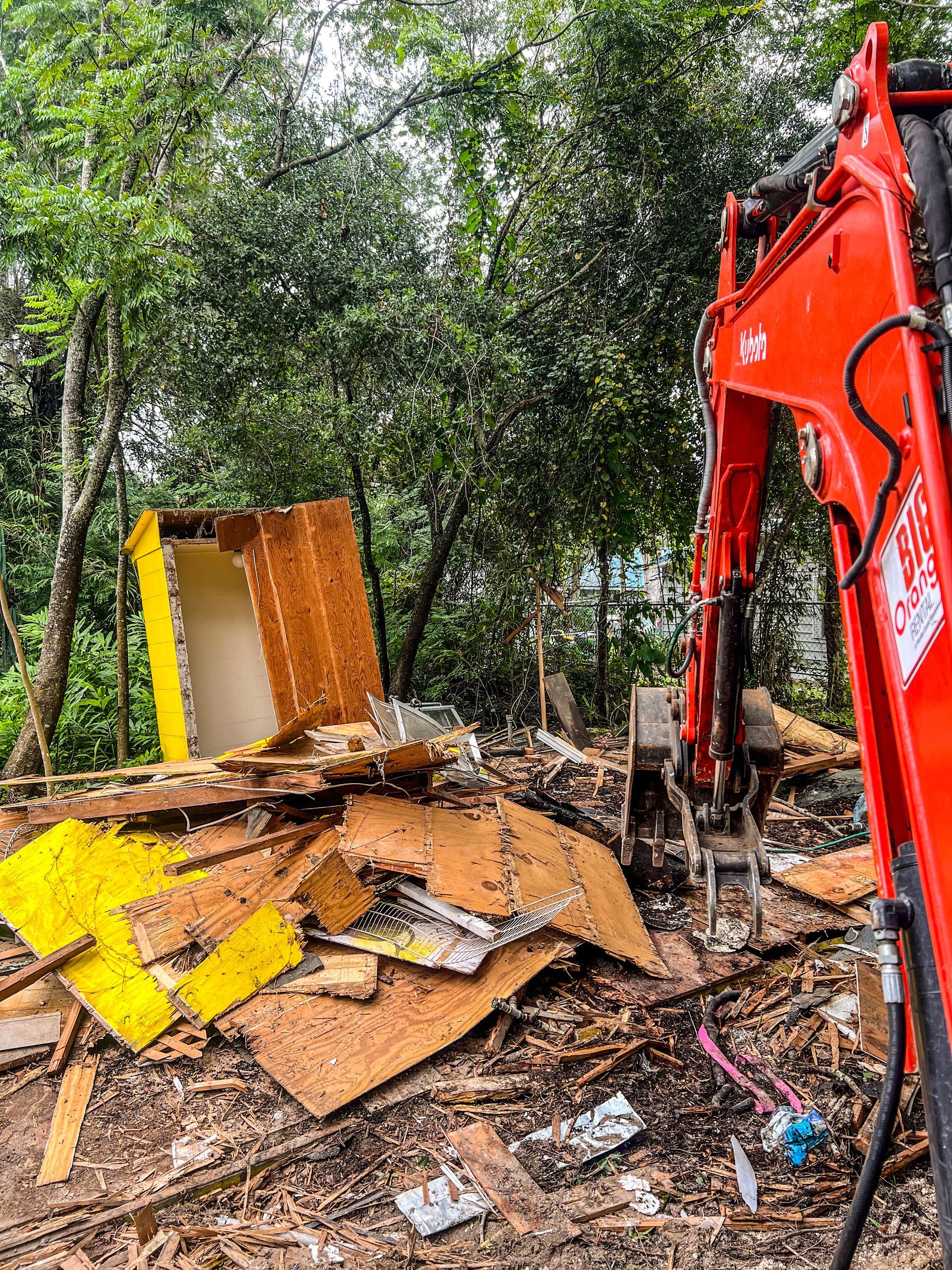 A red excavator is demolishing a building in the woods.