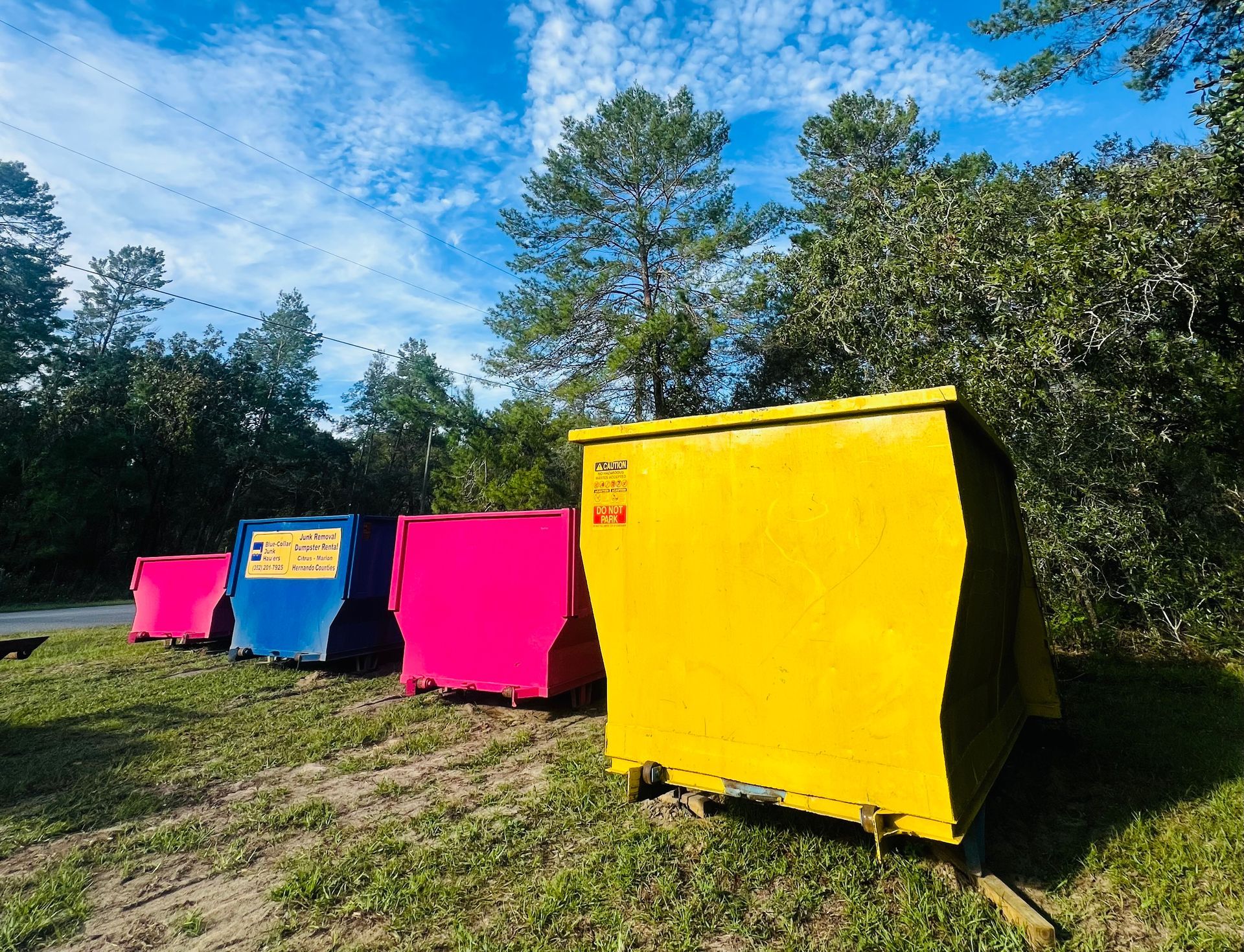A row of colorful dumpsters are parked in a grassy field.
