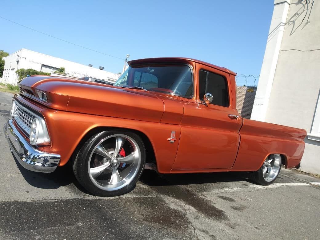 Orange vintage pickup truck parked outside on a sunny day. Chrome wheels and trim.