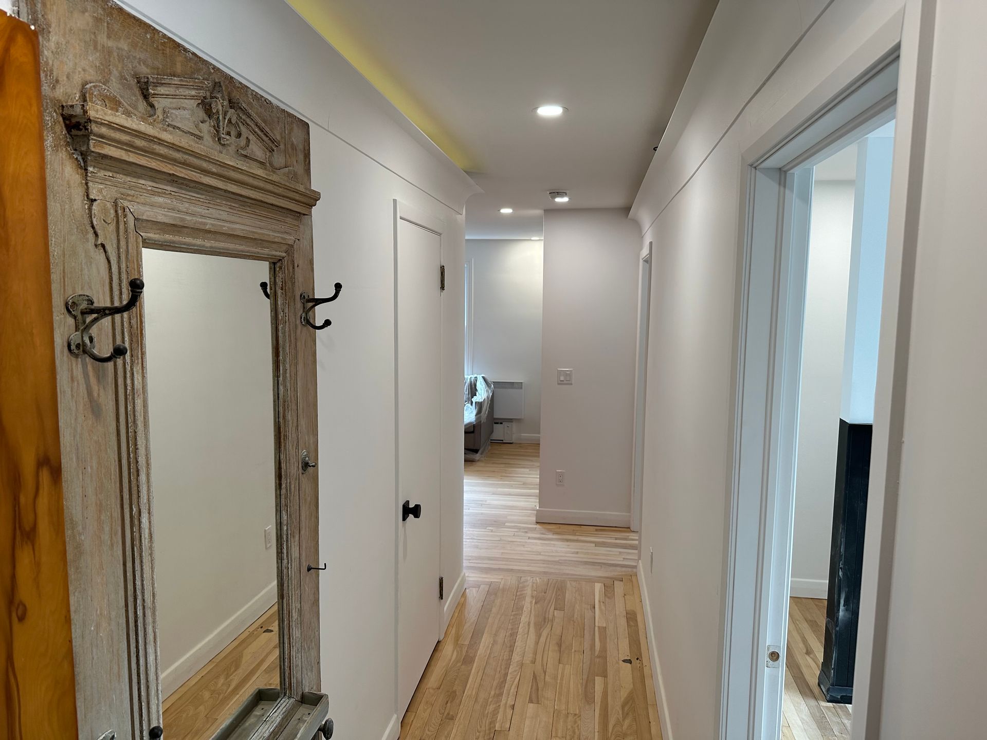 Un couloir avec un miroir au mur et un plancher en bois.