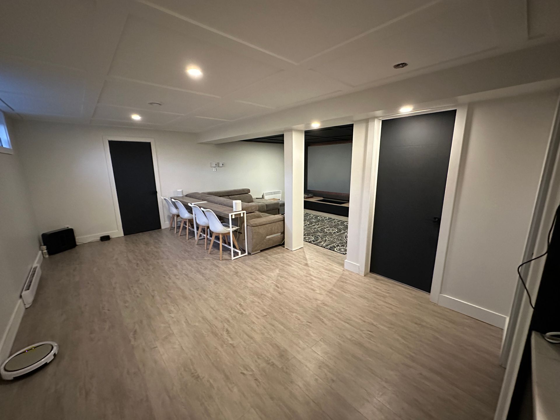 Un salon avec parquet, un canapé, des chaises et une télévision.