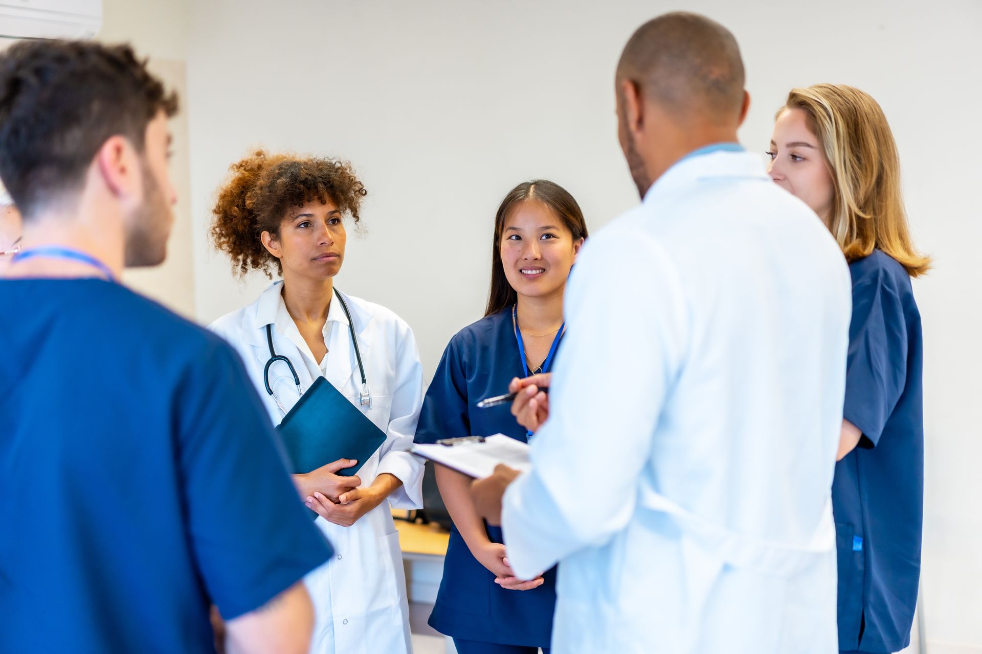Ein Arzt mit Stethoskop lächelt und legt einem Patienten in einem gut beleuchteten Arztzimmer die Hand auf die Schulter.
