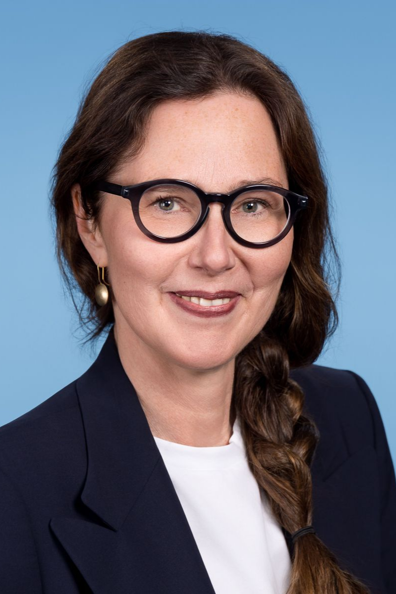 Eine Frau im grünen OP-Kittel lächelt in die Kamera.